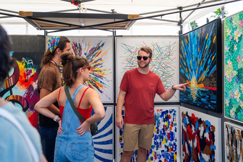 A vibrant art booth with colorful abstract paintings and visitors engaging with the artist.